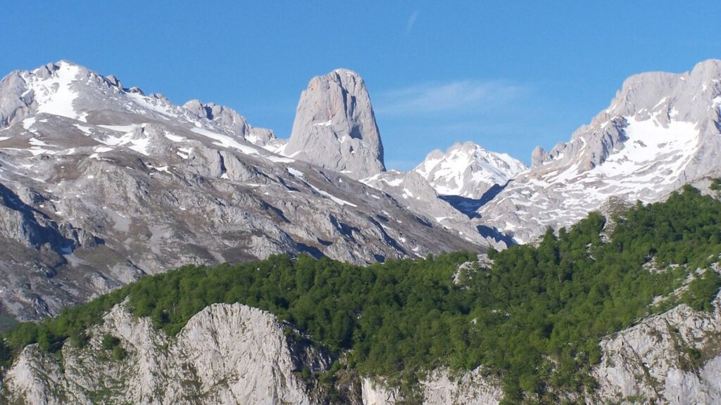 Senderista progresando por un terreno de lapiaces calizos con el Naranjo de Bulnes al fondo.