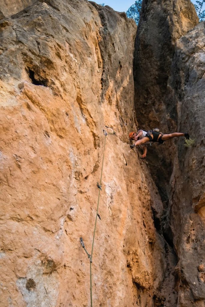 Dos escaladores progresando en una vía de escalada deportiva en roca; uno realiza un movimiento de oposición en un diedro mientras el otro asciende por la sección superior.