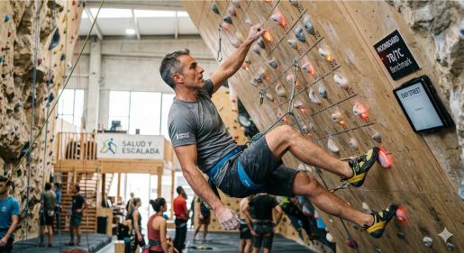 Fotografía real en horizontal de una escaladora segura de primero que ha encontrado un reposo total (sin manos) en roca natural realizando una bandera externa (outside flag) flexionando las piernas para proyectar el centro de gravedad hacia arriba y hacia la pared.