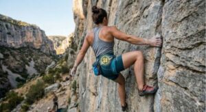 Escaladora con cuerpo real y ancho sacudiendo la mano por debajo del nivel del hombro (shaking) en una placa vertical técnica en vía natural para recuperar pulsaciones encontrando el equilibrio y centro de gravedad.