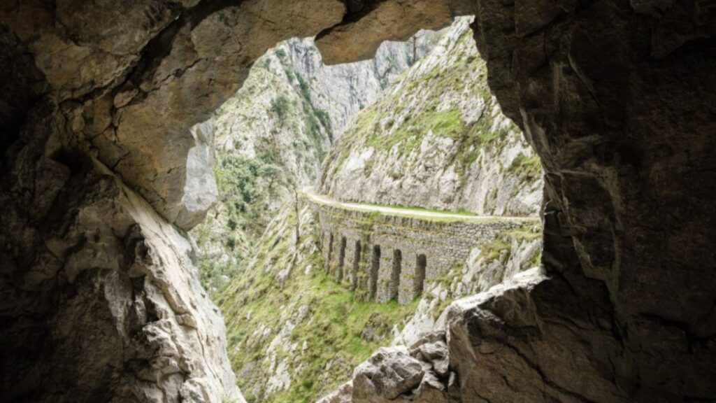 Ruta del Cares en los Picos de Europa despejados, con marcas blancas y amarillas oficiales sobre un poste de madera y un kit de supervivencia minimalista en primer plano, ilustrando la planificación técnica de una travesía.