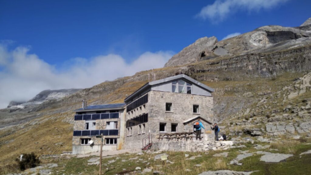 Dos alpinistas equipados se aproximan al Refugio de Góriz en el Parque Nacional de Ordesa, un hito clave de la pernocta en la GR11 Transpirenaica.
