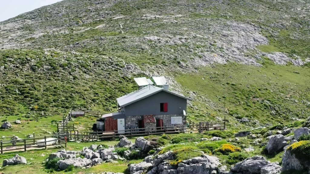 Interior y exterior del Refugio Vega de Ario a 1630 metros, con el Pico Urriellu (Naranjo de Bulnes) visible al fondo bajo un cielo despejado.