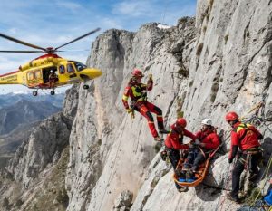 Un equipo de rescate de montaña asiste a un escalador lesionado en una pared de roca, ilustrando por qué es vital federarse en escalada para contar con seguro de accidentes y cobertura de salvamento.
