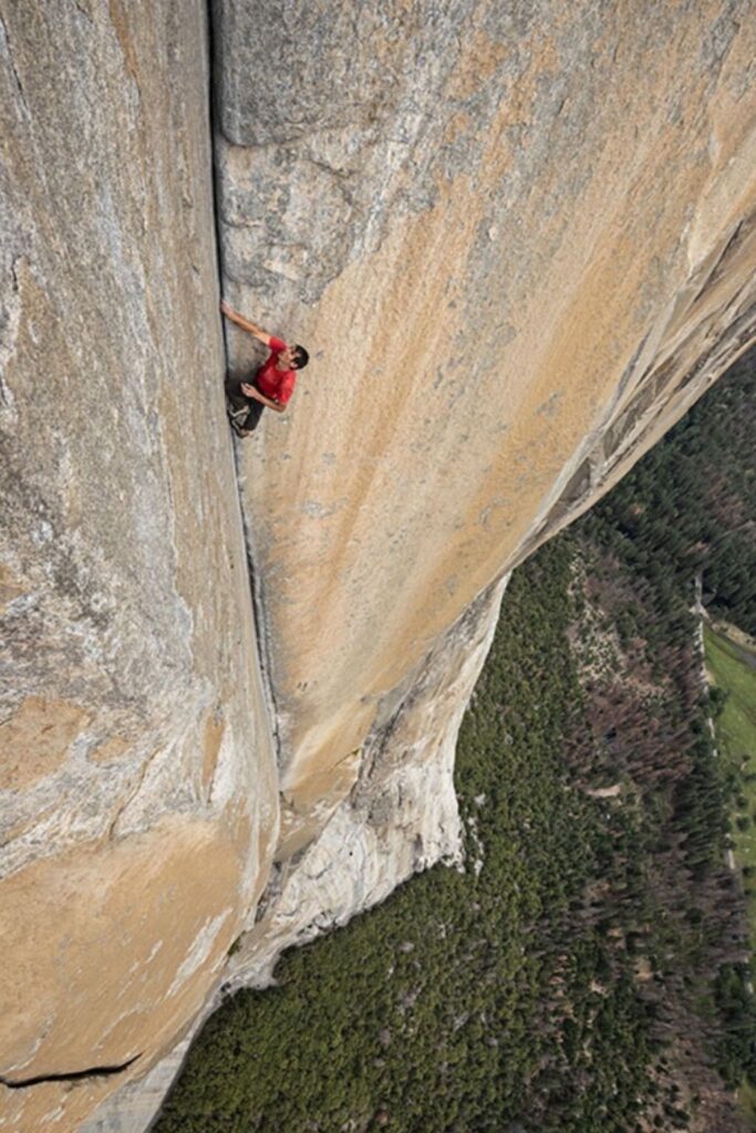 Un escalador realiza una ascensión en free solo por una pared vertical de granito; se observa la ausencia de cuerdas y el uso de pies de gato y magnesio en un entorno de alta exposición.