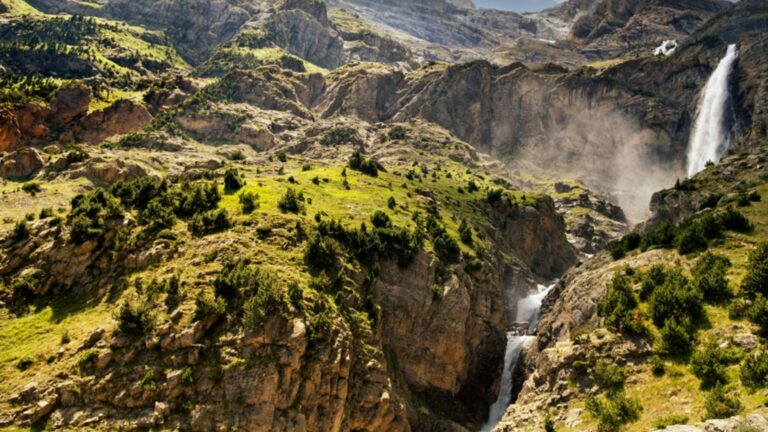 Infografía panorámica de la GR11 Transpirenaica mostrando la transición técnica entre el Circo de Bujaruelo con cascadas y el Ibón de Tebarray con nieve residual y pinares alpinos.
